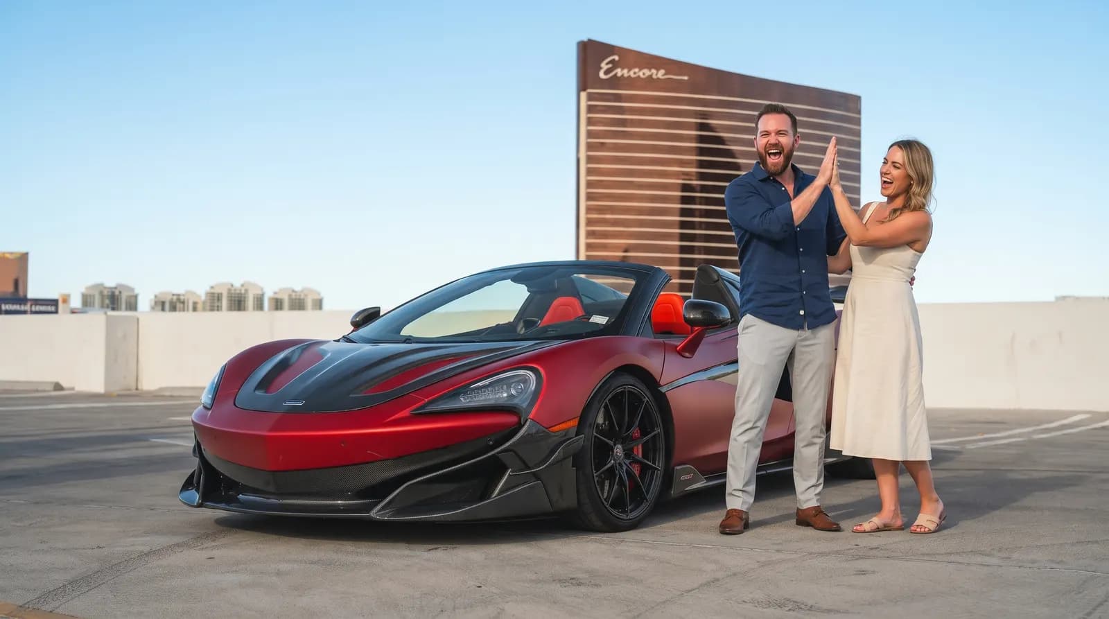 Couple high-fiving beside a matte red McLaren 600LT in Las Vegas